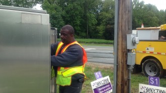 North Carolina Department of Transportation employee Dwaine Evans maneuvers about the power box between North Williamson Ave. and University Drive .